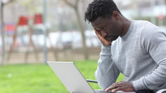 man experiencing burnout, head on hand, string at laptop