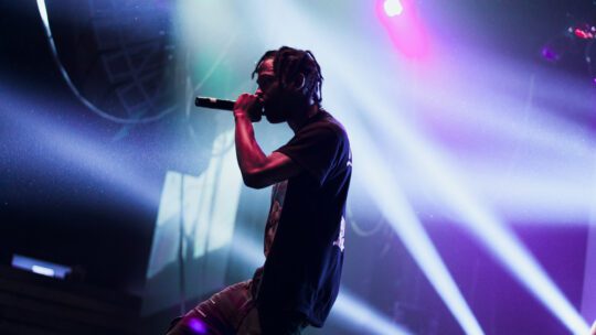 Travis Scott performing at a concert with bright lights