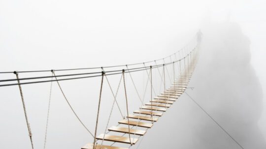 Fuzzy man walking on hanging bridge vanishing in fog.