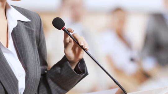 Businesswoman standing on stage and delivering a speech at a podium