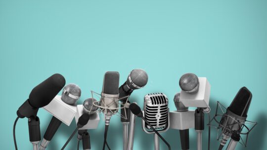 Press conference with standing microphones on an aqua blue background